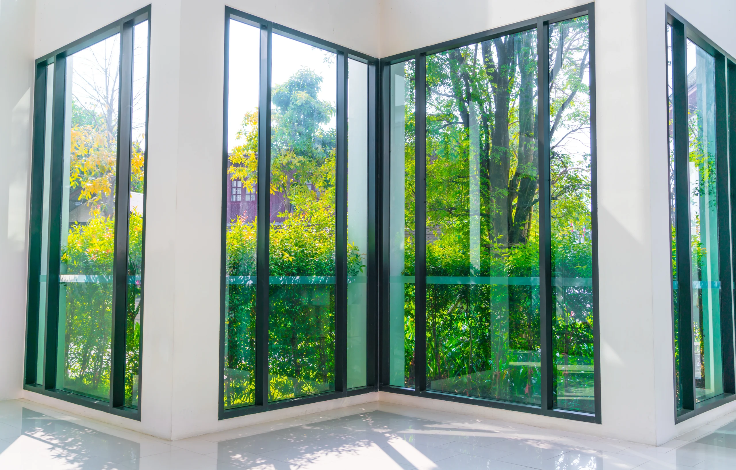Sunlight streams through large floor-to-ceiling modern windows that offer a stunning view of a lush green garden after a fresh Window Installation Covington WA.