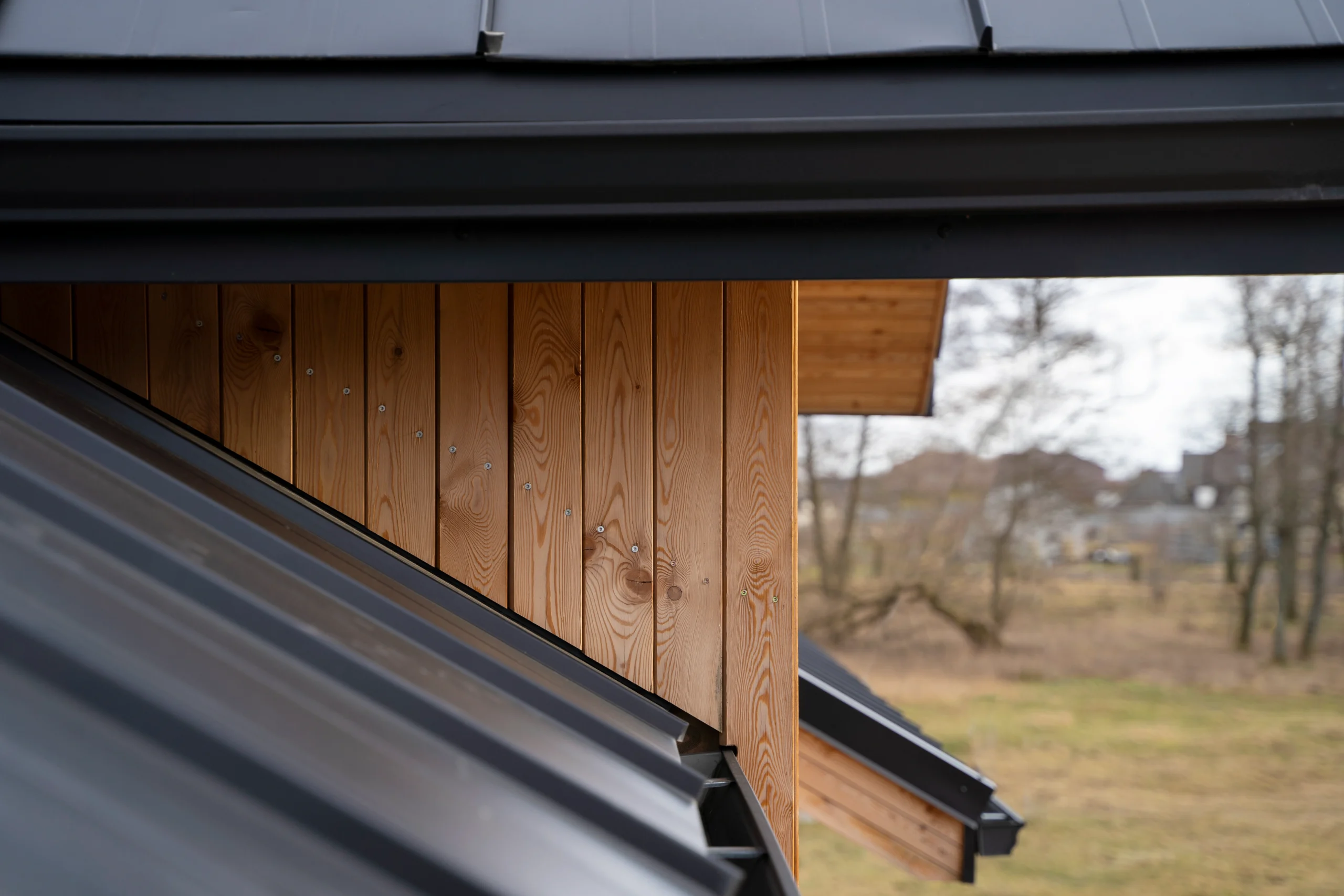 Close-up of a modern black metal roof and vertical natural wooden siding on a contemporary house.