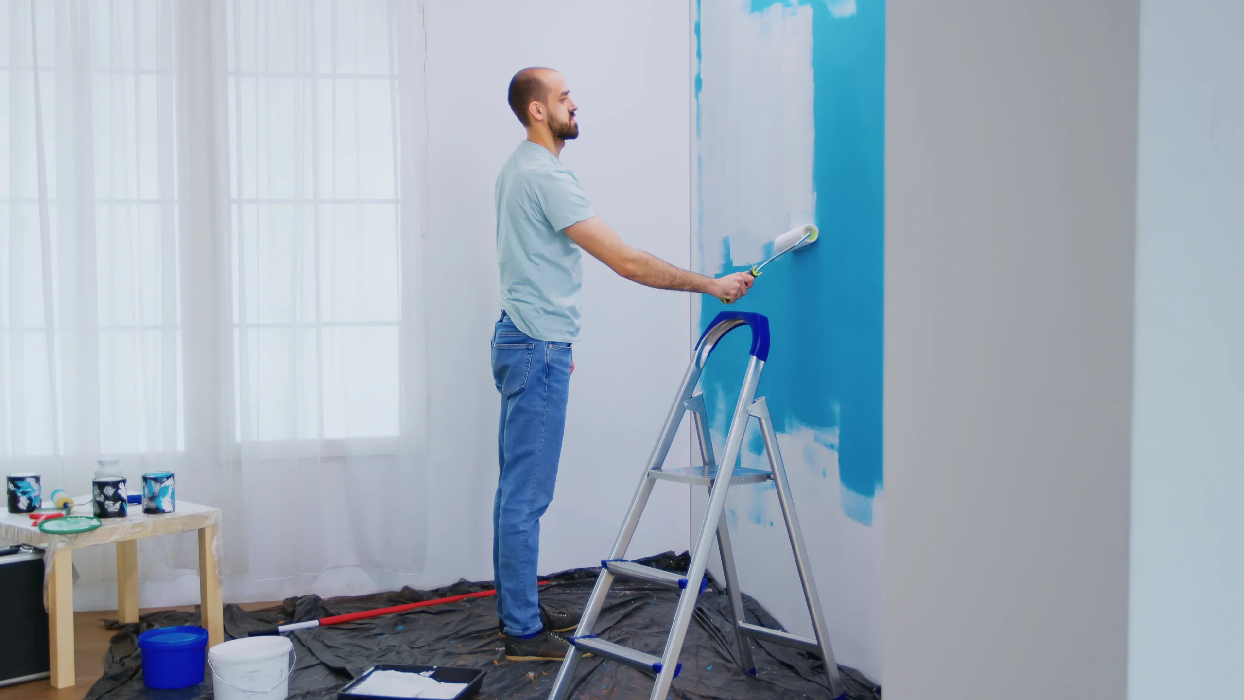 A handyman using a roller to apply white paint over a blue wall, showcasing expert Painting Services Covington WA.
