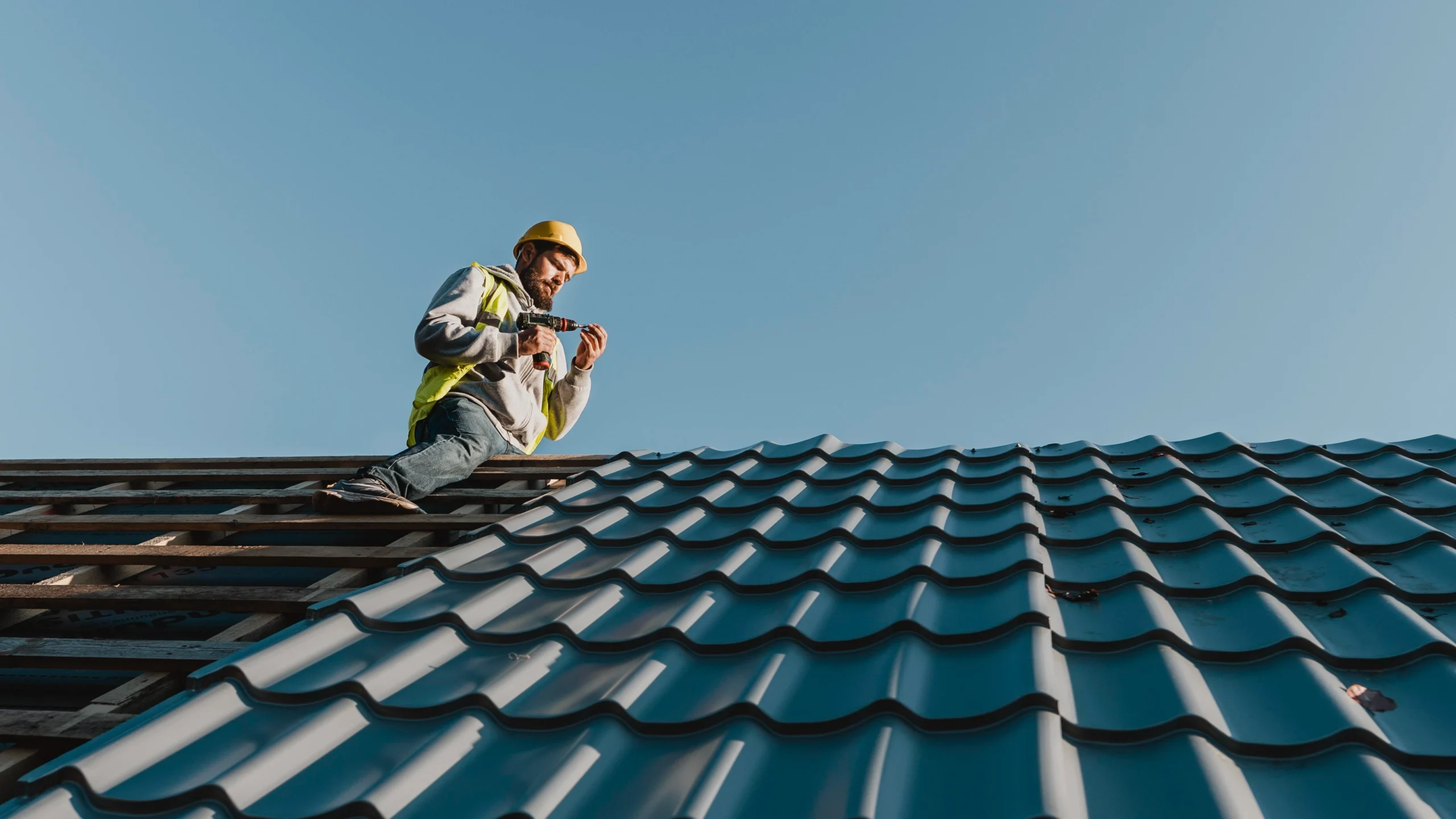 A roofer installs metal tiles during a professional Roof Replacement Covington WA against a clear blue sky.